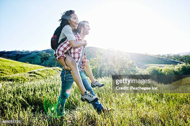 smiling man carrying girlfriend piggyback on hill - active lifestyle los angeles stock-fotos und bilder