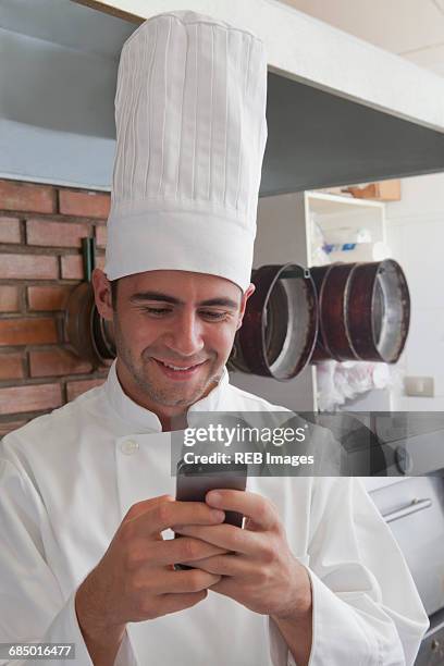 smiling hispanic chef texting on cell phone - oven dial stock pictures, royalty-free photos & images