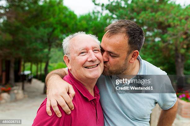 Adult son kissing and hugging his old father