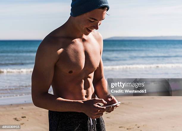 france, crozon peninsula, smiling young man with cell phone on the beach - france crozon peninsula smiling young man with cell phone on the beach stockfoto's en -beelden