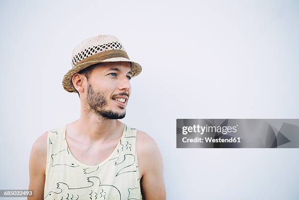 smiling man wearing straw hat and tank top in front of light background - stroh stock-fotos und bilder