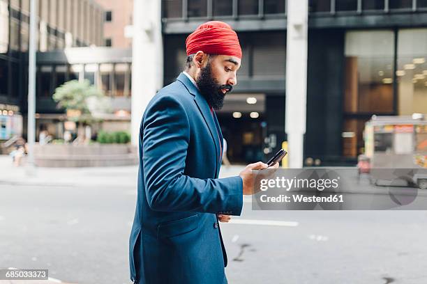 indian businessman in manhattan using smartphone, walking in the street - sikhisme stockfoto's en -beelden