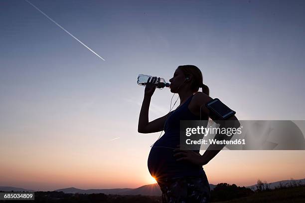 silhouette of pregnant woman drinking water from bottle at sunset - sunset with jet contrails stock pictures, royalty-free photos & images