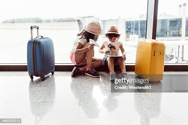 two little girls waiting at airport, playing with digital tablet - airport family stock-fotos und bilder