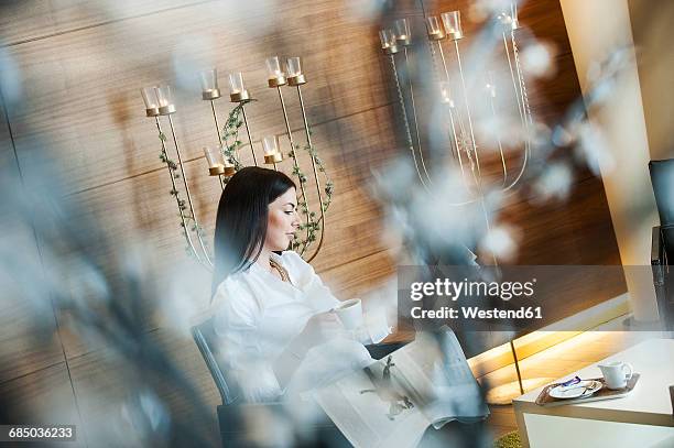reading woman sitting in hotel lounge, drinking coffee - newspaper luxury stock-fotos und bilder