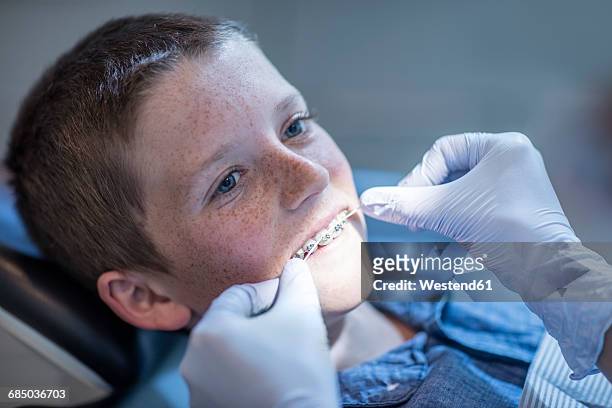 boy with braces in dental surgery receiving dental floss treatment - kids with cleaning rubber gloves stock-fotos und bilder