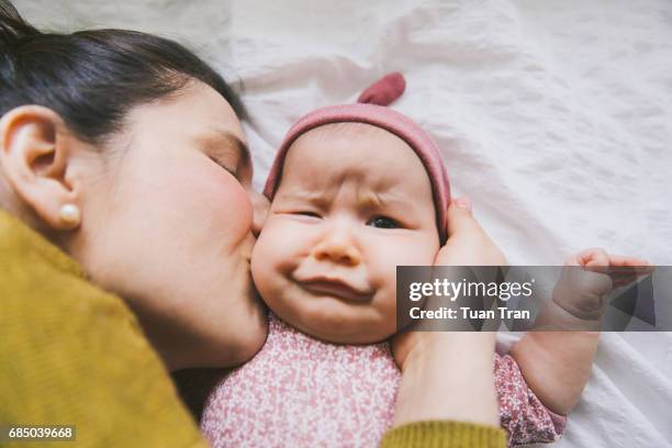 baby making funny face when mother kiss - baby eltern von oben stock-fotos und bilder