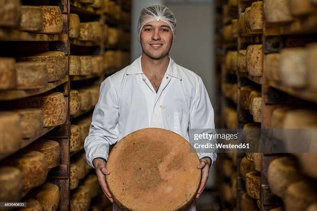 Cheese factory worker proudly holding loaf of cheese