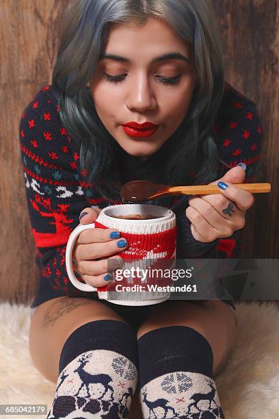 young woman wearing patterned knit pullover and overknees enjoying hot chocolate in front of wooden wall - regarder vers le bas photos et images de collection
