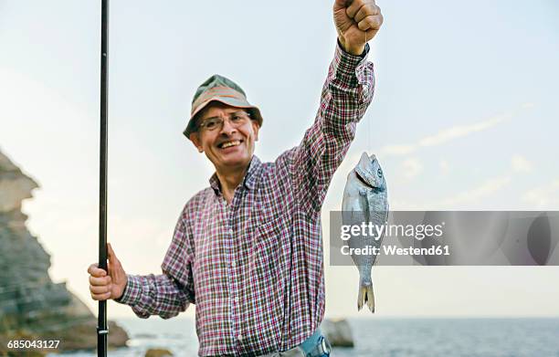 happy senior man holding fish on fishing line - fang stock-fotos und bilder