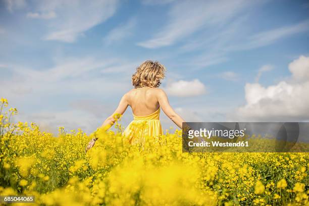 back view of blond woman wearing yellow dress standing in rape field - robe jaune photos et images de collection