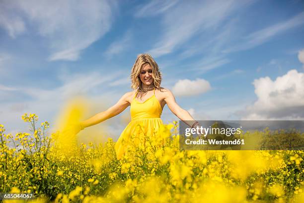 happy blond woman wearing yellow dress standing in rape field - brassica - fotografias e filmes do acervo