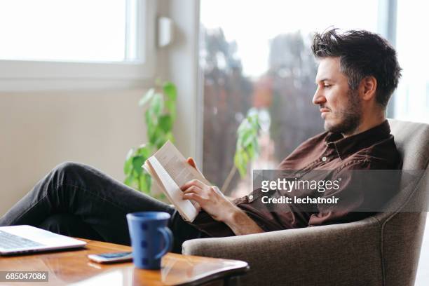 young man reading a book at home - reading stock pictures, royalty-free photos & images