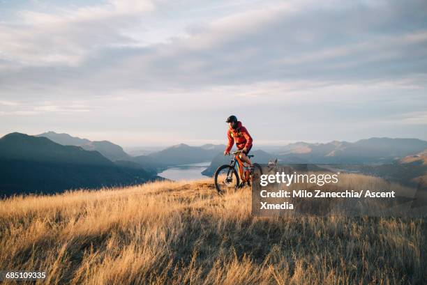 mountain biker ascends mountain ridge, with dog - mountain biking fotografías e imágenes de stock