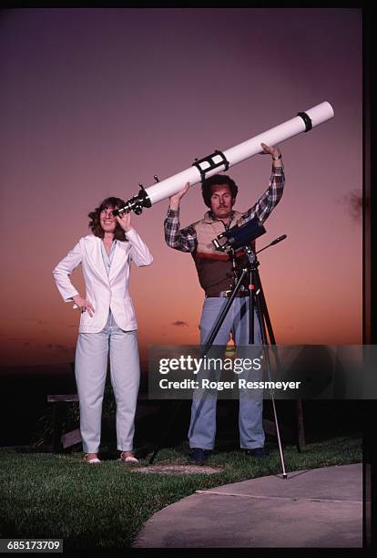 Amateur astronomer Doug Berger holds a refracting telescope over his head while his wife looks through it.