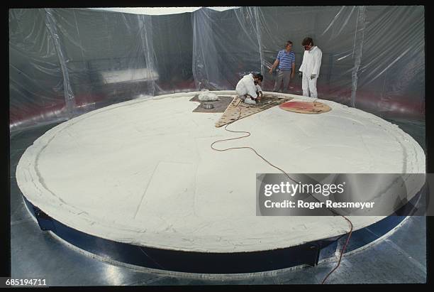 Workers lay hearth plates on a turntable inside a large oven at the Steward Observatory Mirror Laboratory in Arizona. Glass will be melted and spun...