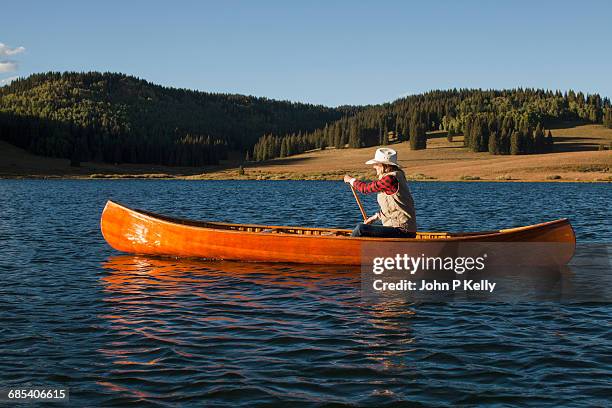 young woman paddles vintage wooden canoe on a lake - rowing boat stock pictures, royalty-free photos & images