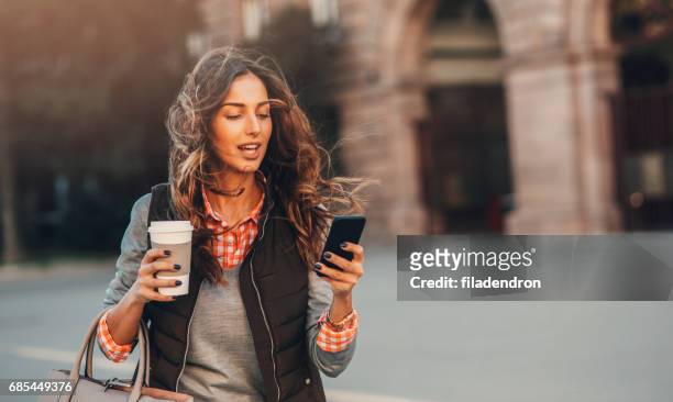 woman texting and drinking coffee outdoors. - on the move stock pictures, royalty-free photos & images
