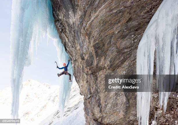 man hanging on ice axe while climbing on frozen rock wall - frozen waterfall stock pictures, royalty-free photos & images