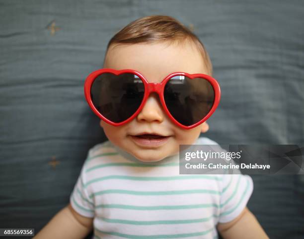 a 8 months old baby boy wearing heart shaped glasses - baby in sunglass stockfoto's en -beelden