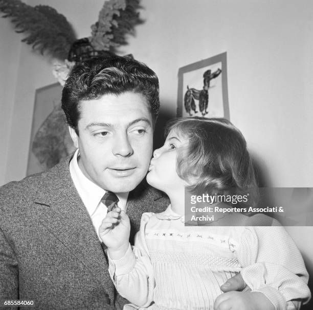 Italian actor Marcello Mastroianni with his daughter Barbara, kissing him on his cheek, during a photoshooting at home. Italy, 1955