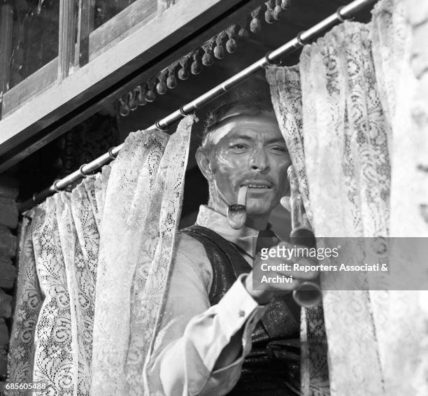 American actor Lee Van Cleef standing at the window holding a telescope in a scene from the film 'For a Few Dollars More', directed by Sergio Leone,...