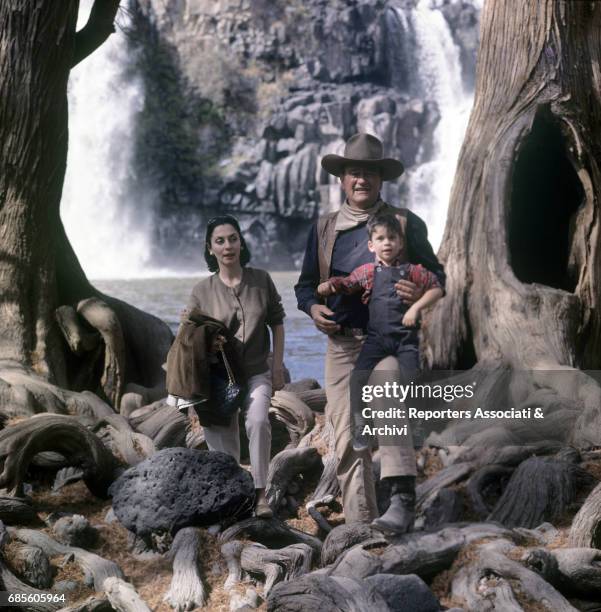 American actor and director John Wayne being photographed with his son Ethan and his wife Pilar Pallete during a break on the set of the film 'The...