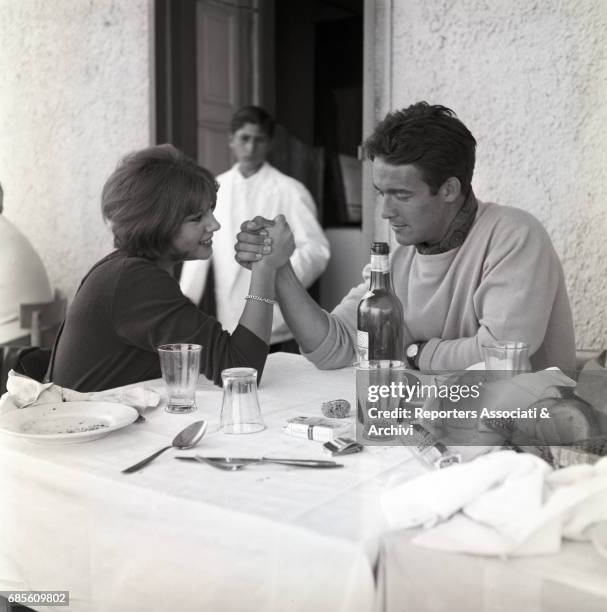 Italian actress Stefania Sandrelli and French actor Jacques Charrier doing arm wrestling in a restaurant. 1965