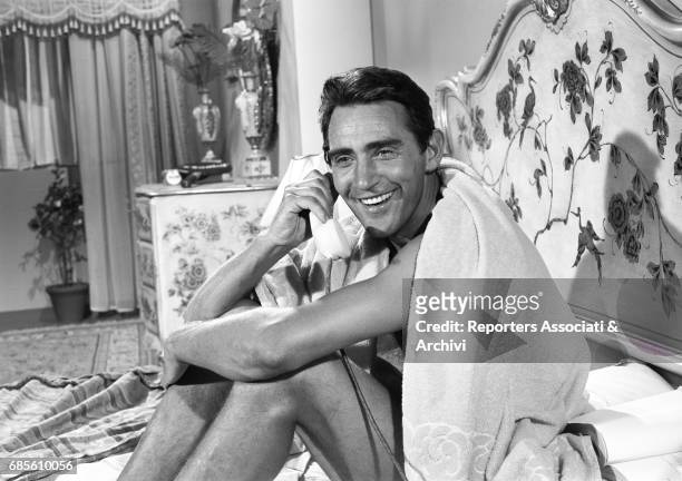 Italian actor, comedian and TV host Walter Chiari sitting on the bed and speaking over the phone in a scene from the film 'Caccia al marito' directed...