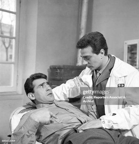 Italian actor, comedian and TV host Walter Chiari lying on a bed to be examined by a Lieutenant Doctor in a scene from the film 'Obiettivo ragazze'...
