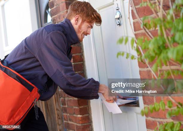 postman posting letters through resident's door - postbode stockfoto's en -beelden