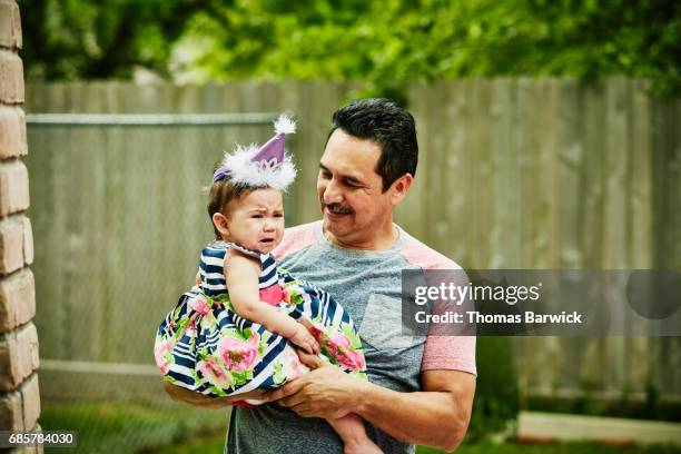 smiling grandfather holding crying granddaughter during first birthday party - first birthday 個照片及圖片檔