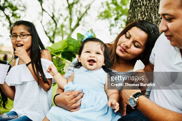 Laughing infant girl with chocolate on face sitting on mothers lap during birthday party