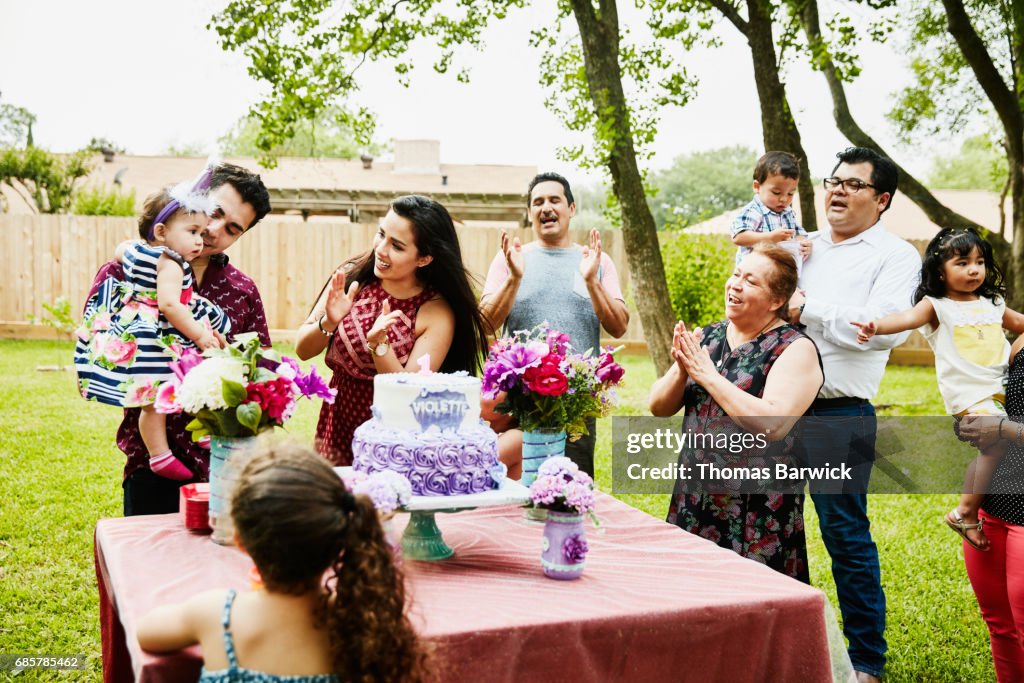 Family singing happy birthday in backyard to young girl on first birthday
