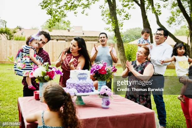 family singing happy birthday in backyard to young girl on first birthday - eerste verjaardag stockfoto's en -beelden