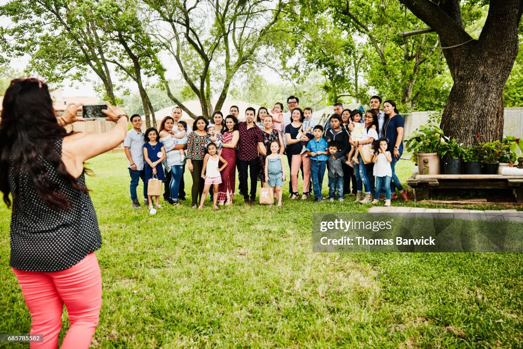 Woman taking photo of smiling multigenerational family gather for backyard birthday party
