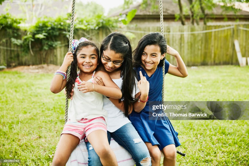 Three laughing female cousins swinging on swing in backyard