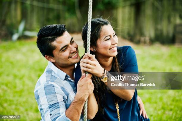 smiling woman sitting on husbands lap on swing during backyard party - zwaaien activiteit stockfoto's en -beelden