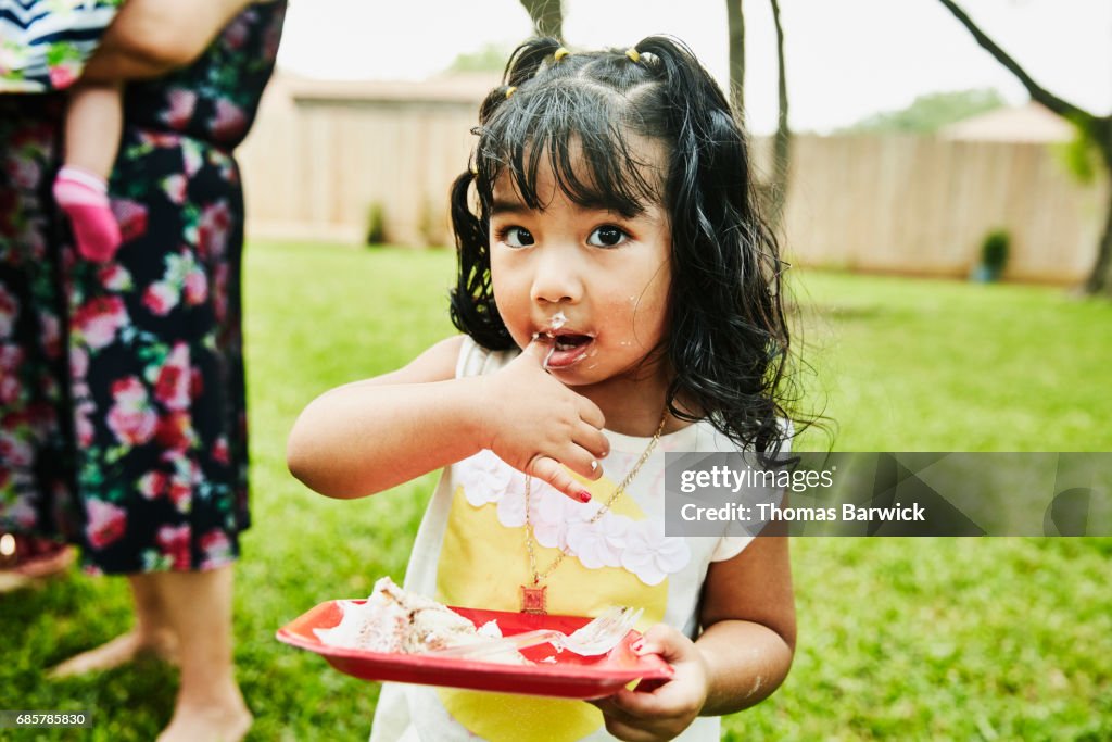 Young girl with frosting on face eating cake during family birthday party