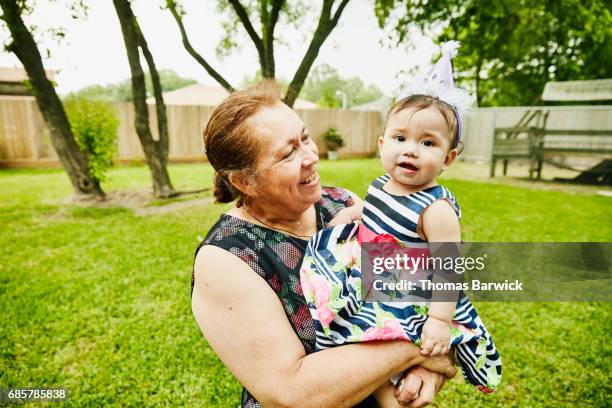smiling grandmother holding granddaughter during her first birthday party - hispanic grandmother stock pictures, royalty-free photos & images