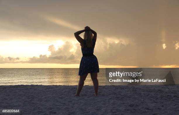 woman standing on the beach pauses by the seashore - female looking away from camera serious thinking outside natural stock-fotos und bilder