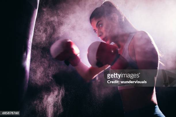 young woman training with boxing gloves and a punching bag - mixed martial arts stock pictures, royalty-free photos & images