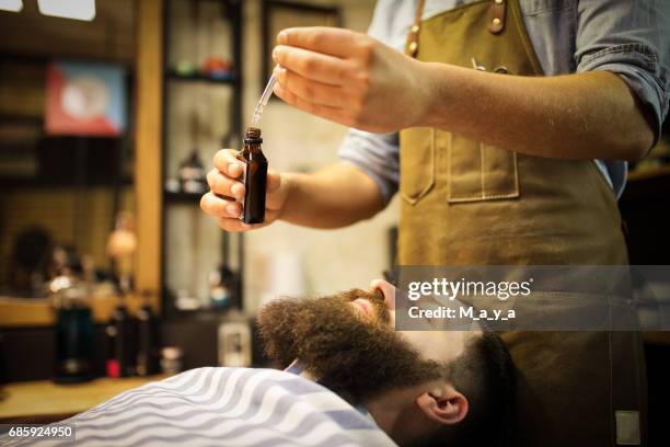 barber putting beard oil to client - beard stock pictures, royalty-free photos & images