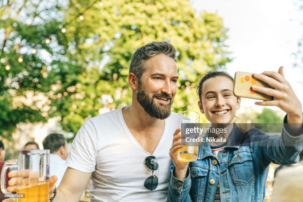Glücklicher Vater mit Tochter im Teenageralter nehmen Selfie im Biergarten