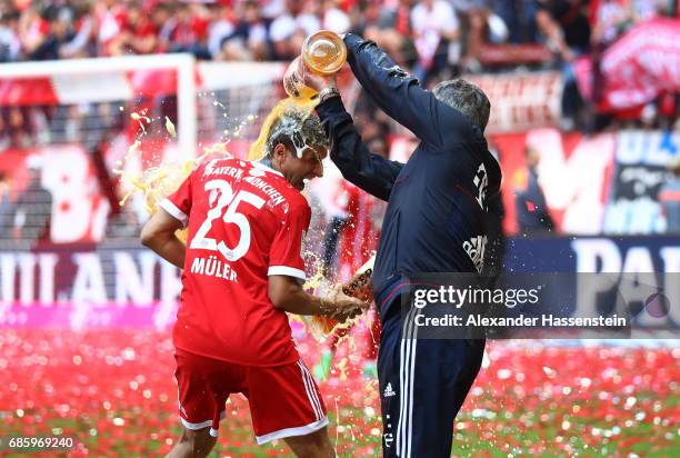 Thomas Mueller of Bayern Muenchen and Carlo Ancelotti, Manager of Bayern Muenchen shower each other in beer following the Bundesliga match between...