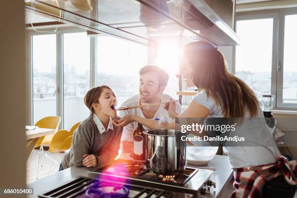 mutter kochen und geben ihrer tochter zu versuchen - kochlöffel stock-fotos und bilder