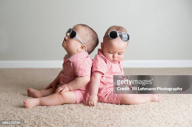 11 month old fraternal twin boys play together with sunglasses - twin babies stockfoto's en -beelden