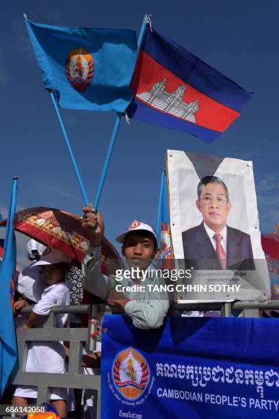 Supporter of Cambodian People Party holds a National flag and a party flag next to a portrait photo of Cambodia's Prime Minister Hun Sen during the...