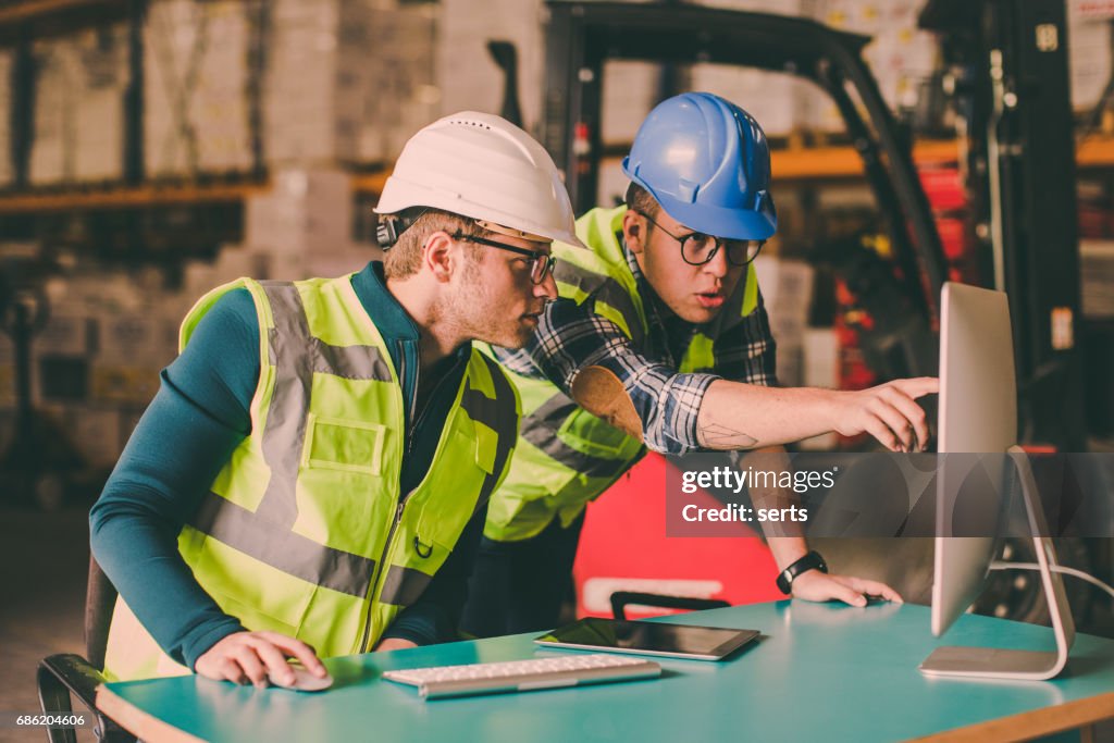 Manual worker and engineer using computer in shipping warehouse