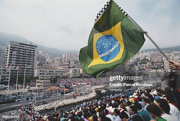 Spectators wave a Brazilian flag from the grandstand overlooking the harbour as Ayrton Senna of Brazil drives the Honda Marlboro McLaren McLaren...